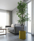 A modern living room with a gray couch, a coffee table, and a tall plant in a yellow planter pot. The room has large windows and concrete walls.