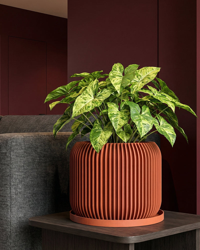 A terracotta planter pot with a diamond pattern holds a green plant on a marble-topped side table next to a gray sofa with a cream-colored throw.