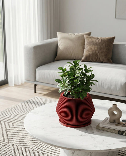 A red planter pot with a Venus flytrap plant inside sits on a light wood console table in front of a large window with a city view. The pot has a ribbed design and a flared base. A geometric metal sculpture and a white lamp are also on the table. The room has a modern, minimalist aesthetic with concrete walls and large windows.