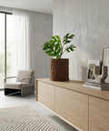 A brown textured planter pot with a green plant sits on a light wood cabinet in a modern living room.