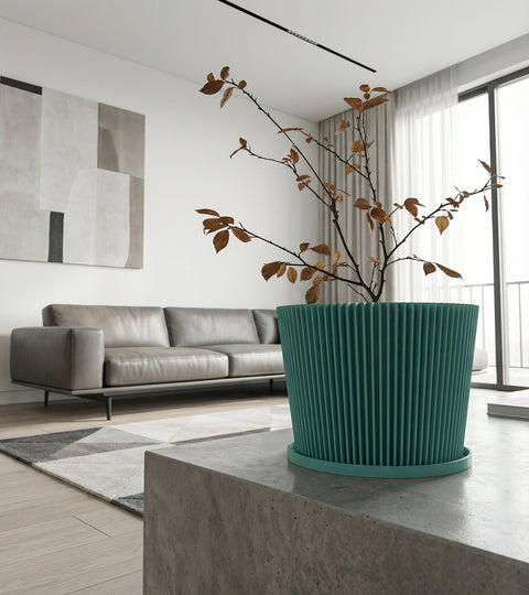 A teal planter pot with a plant sits on a dark wooden table next to a gray couch with a blanket.