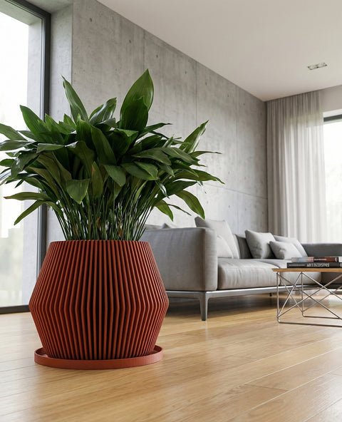 A close-up shot showcases a vibrant green plant nestled in a terracotta-colored planter pot. The pot features a unique vertical ribbed design, adding texture and visual interest. The plant and pot are placed on a wooden surface, with a large window providing natural light in the background. A minimalist shelf with decorative objects is visible in the corner, complementing the modern interior design.