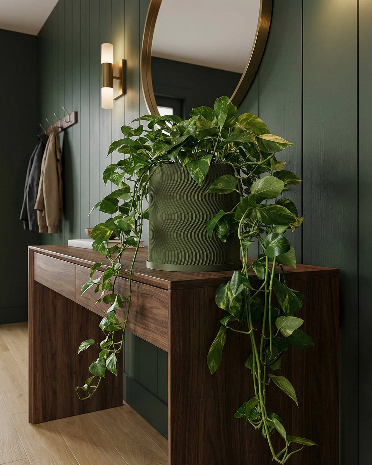 A green planter pot with a wavy design sits on a wooden table, overflowing with a lush, leafy plant.