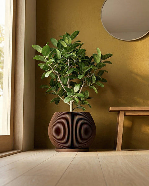 A modern living room features a large Alocasia plant in a unique, vertically-slatted wooden planter pot. The pot is brown and sits on a matching saucer. In the background, a wooden cabinet, a geometric wall art, and large windows with sheer curtains add to the room's contemporary aesthetic.