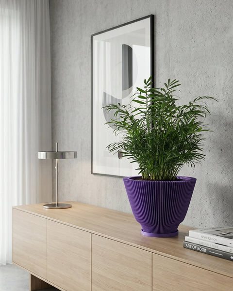 A vibrant purple planter pot sits atop a light wood cabinet, showcasing a lush green plant. A modern lamp and framed artwork add to the stylish interior. The planter's unique ribbed design complements the room's contemporary aesthetic.