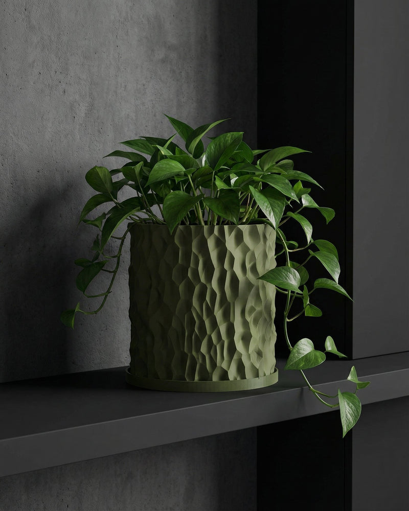 A green pothos plant in a textured green planter pot sits on a dark gray shelf against a gray wall.