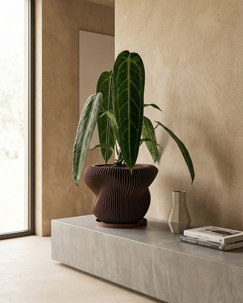 A planter pot with a plant in it sits on a wooden table next to a small sculpture. The planter pot is brown and has a unique design.