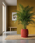 A red planter pot with a green plant sits on a woven rug in a room with a yellow wall.
