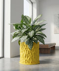 A vibrant yellow planter pot with a textured surface, holding a lush green plant with silver-striped leaves, sits on a gray floor in a bright, modern room.