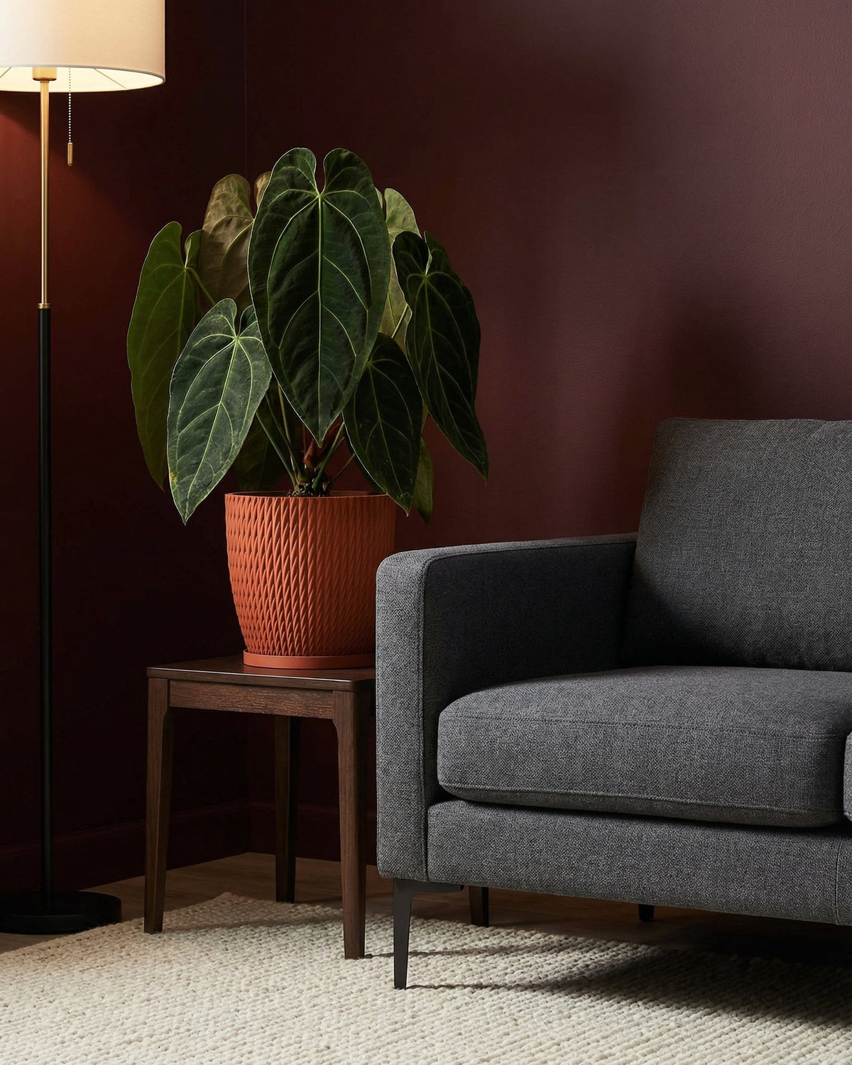 A planter pot with a plant sits on a table next to a gray couch and a lamp. The planter pot is orange and has a textured design.