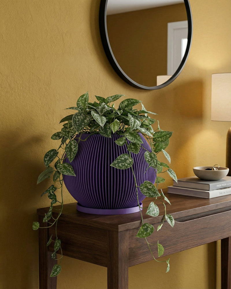 A vibrant purple planter pot sits atop a light wood cabinet, showcasing a lush green plant. A modern lamp and framed artwork add to the stylish interior. The planter's unique ribbed design complements the room's contemporary aesthetic.