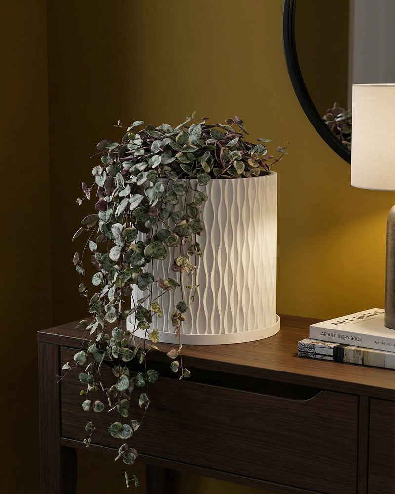 A string of pearls plant spills from a white, textured planter pot on a wooden console table in a room with dark green walls.