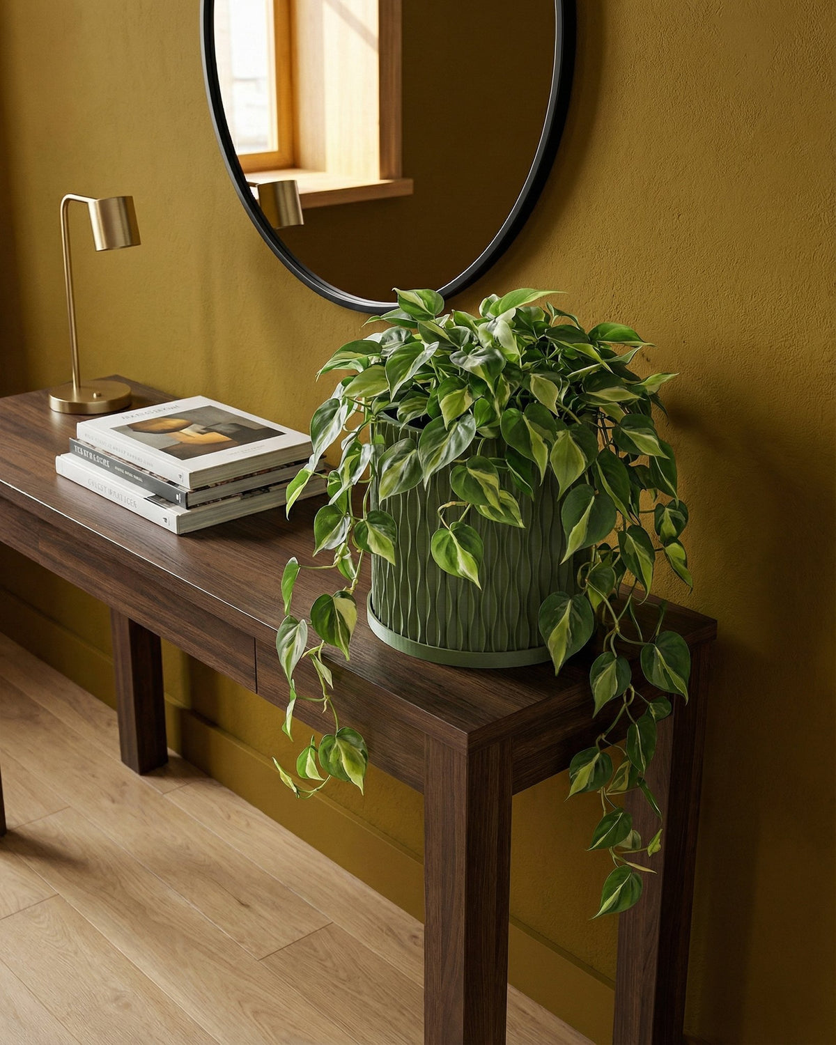 A green planter pot with a plant sits on a wooden table in a room with a rug and a basket hanging on the wall.