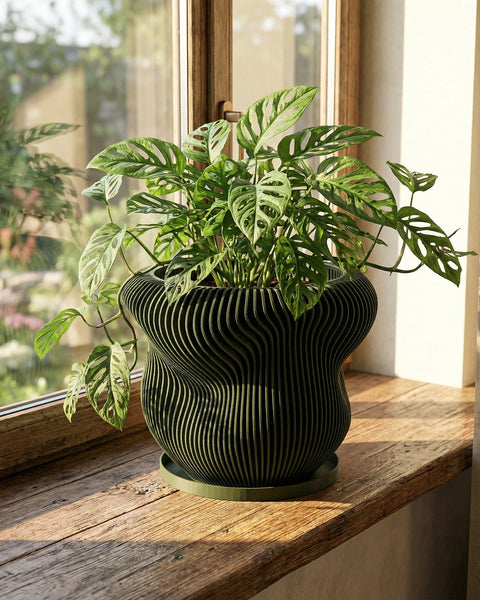 A green planter pot with a plant inside sits on a concrete surface next to a stack of books and a wooden stool.