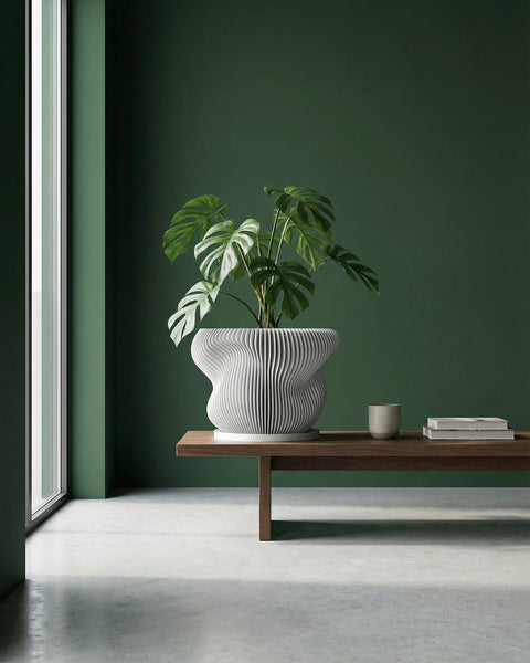 A Monstera plant in a white, vertically ribbed planter pot sits on a wooden table next to a gray couch.