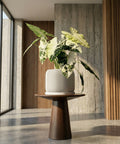A white planter pot with a green plant sits on a dark wood table in a room with red walls.