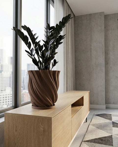A variegated plant in a brown textured planter pot sits on a wooden cabinet against a mustard-colored wall.