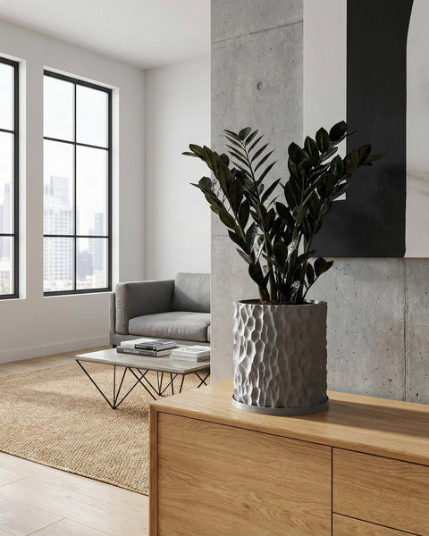 A gray planter pot with a textured surface sits on a wooden cabinet in a modern living room. The pot holds a green plant.