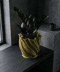 A vibrant pothos plant cascades from a textured, olive-green planter pot, sitting on a dark wood surface.