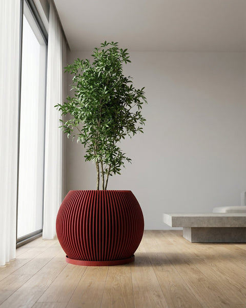 A red, round, ribbed planter pot with a green plant inside is placed on a wooden floor in a room with a window.