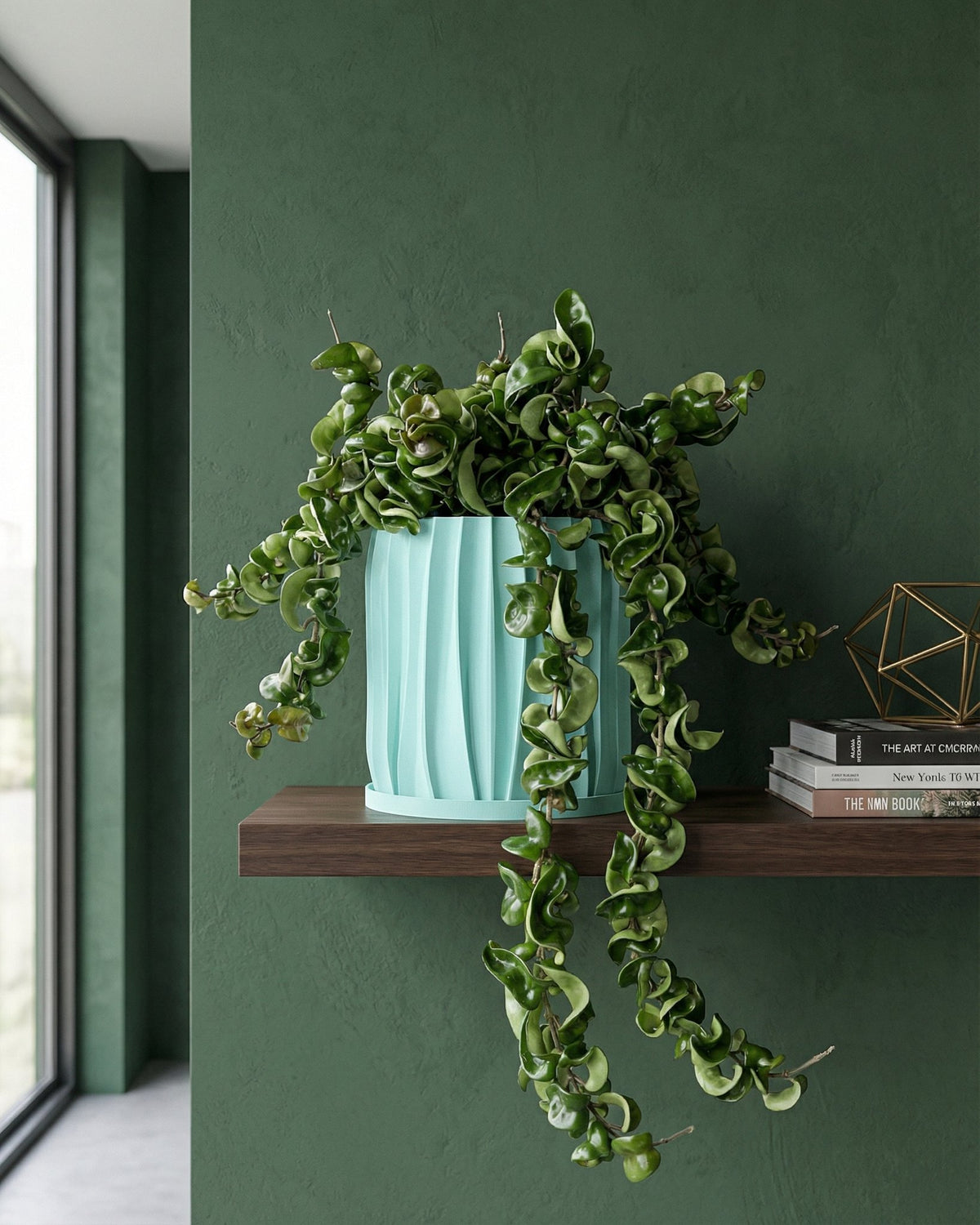 A turquoise planter with a trailing plant sits on a wooden table in a hallway with dark green walls and a jute rug.