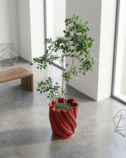 A red planter pot with a textured surface sits on a gray floor, holding a small tree with green leaves. A wooden cabinet is nearby.