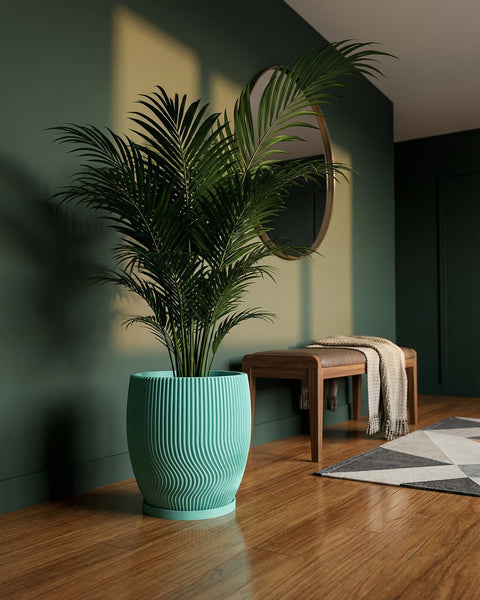 A vibrant green palm in a wavy, textured planter pot sits on a shiny wood floor in a room with green walls.