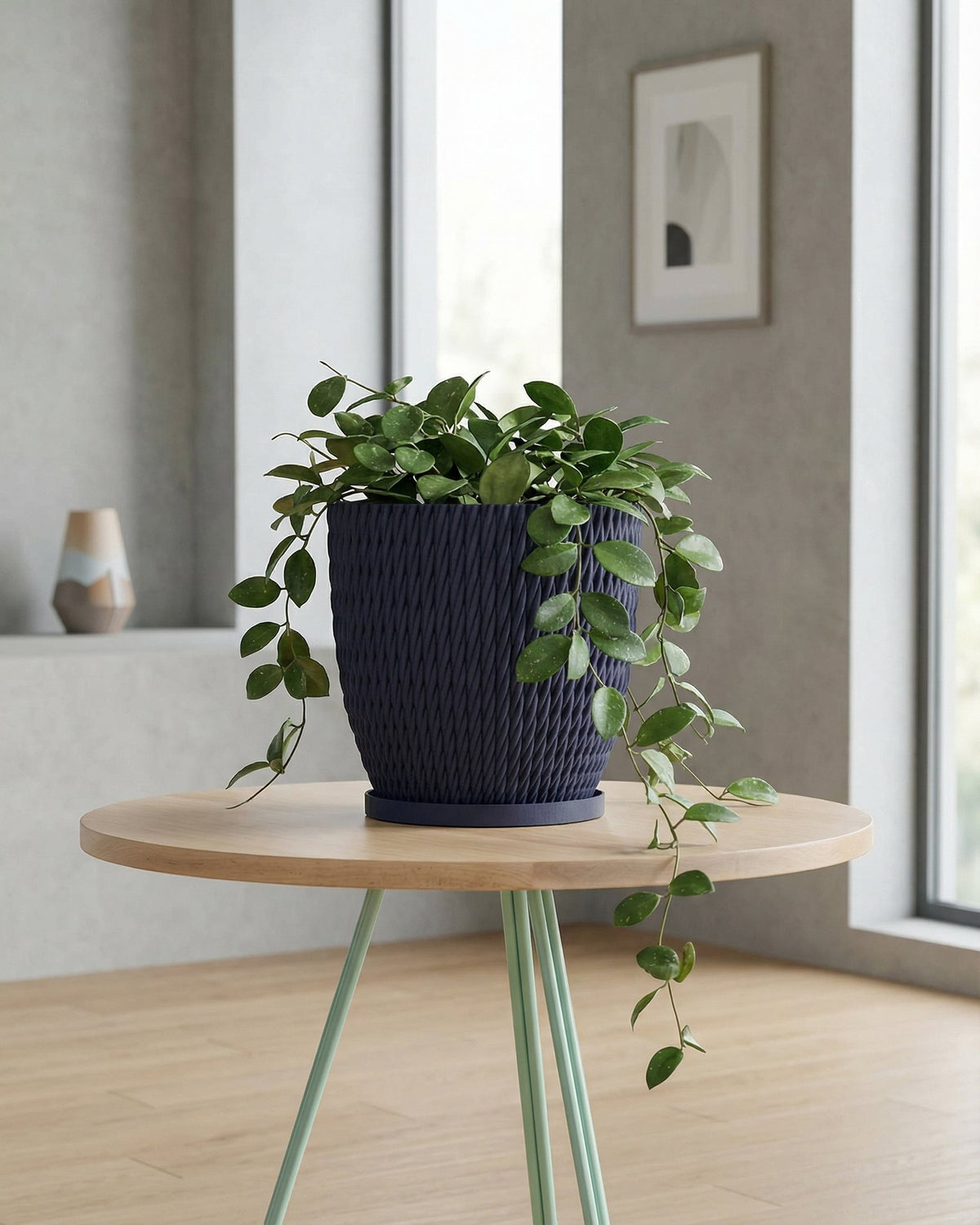 A navy blue planter pot with a green plant on a wooden table with green legs.