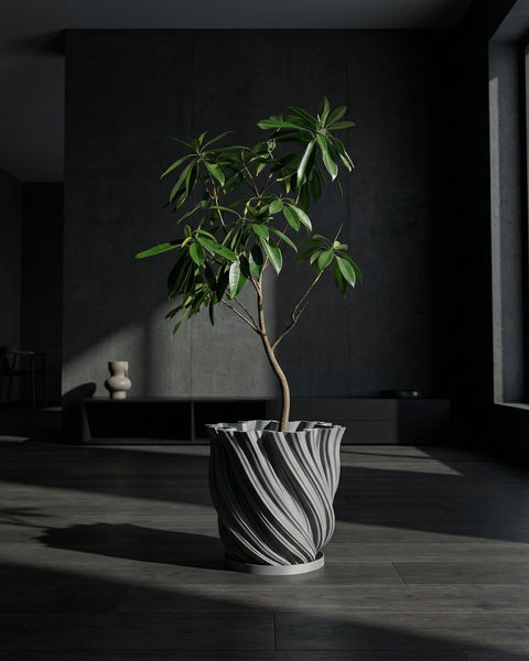A gray planter pot with a textured, swirling design sits next to a light gray sofa with pillows and a throw blanket. A green plant is in the pot.
