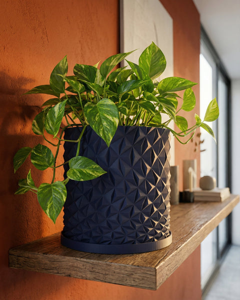 A pothos plant in a navy blue planter with a geometric design sits on a wooden shelf against an orange wall.