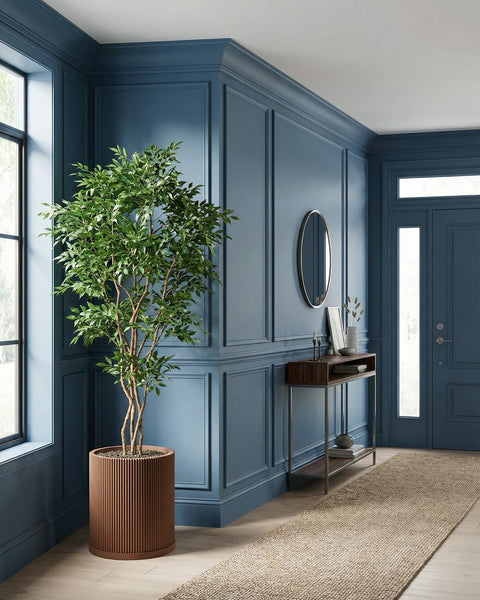 A brown, ribbed planter pot with a green tree inside sits in a blue entryway with a rug and console table.