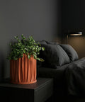 A fiddle leaf fig plant in a textured orange planter pot sits on a wooden table against a green wall.