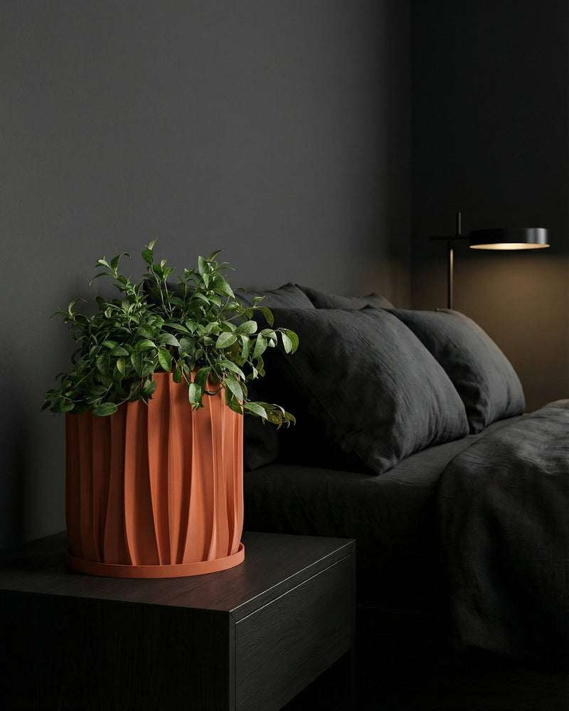 A fiddle leaf fig plant in a textured orange planter pot sits on a wooden table against a green wall.
