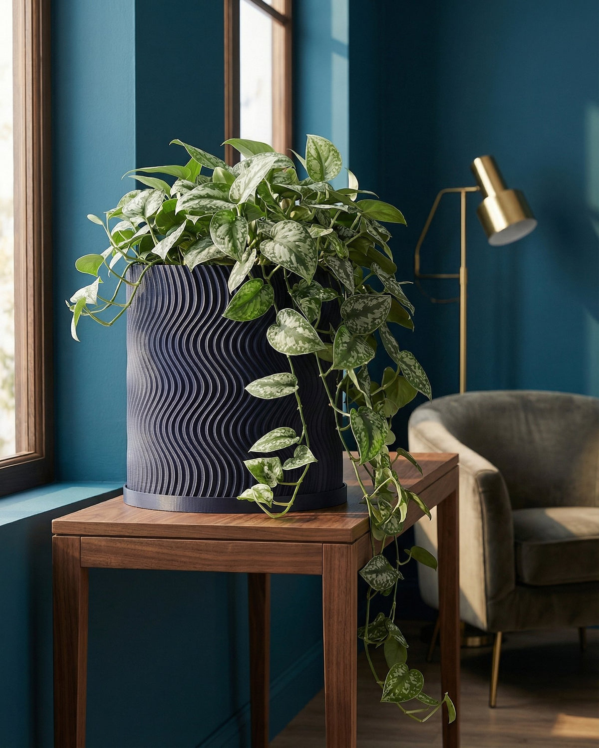 A pothos plant in a navy blue planter pot sits on a wooden table in a room with blue walls.