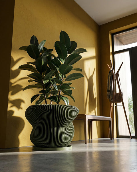 A green planter pot with a plant on a wooden table, next to a gray couch and a green wall.