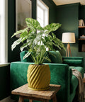 A vibrant indoor scene featuring a lush green plant in a stylish yellow planter pot, set on a rustic wooden table against a backdrop of a green sofa.