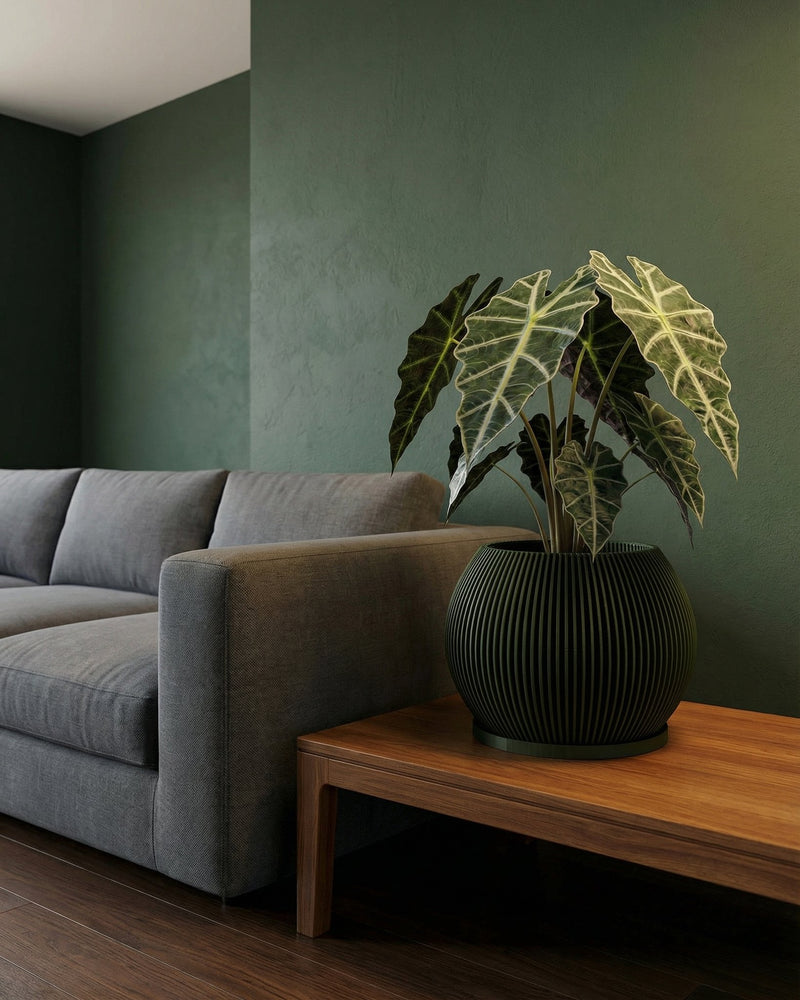 A green planter pot with a plant on a wooden table, next to a gray couch and a green wall.