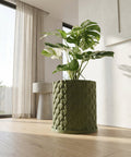 A green planter pot with a plant in it sits on a dark gray shelf against a dark gray wall.