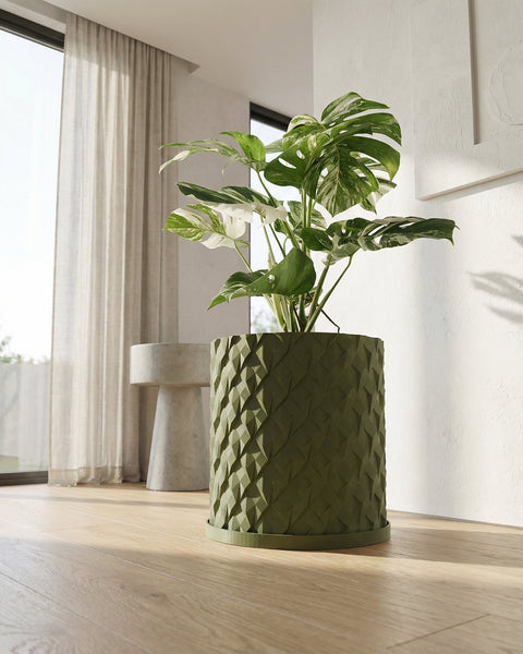 A green planter pot with a plant in it sits on a dark gray shelf against a dark gray wall.