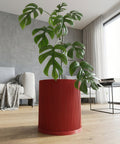 A red, ridged planter pot with a green plant inside sits on a light wood floor in a modern living room.