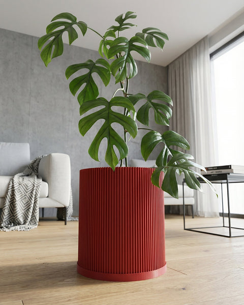 A red, ridged planter pot with a green plant inside sits on a light wood floor in a modern living room.