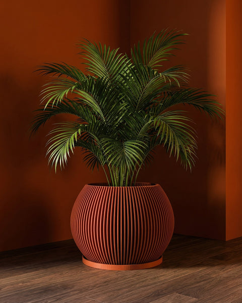 A vibrant green palm plant sits in a modern, orange-toned, vertically-striped planter pot on a wooden floor against a matching orange wall.