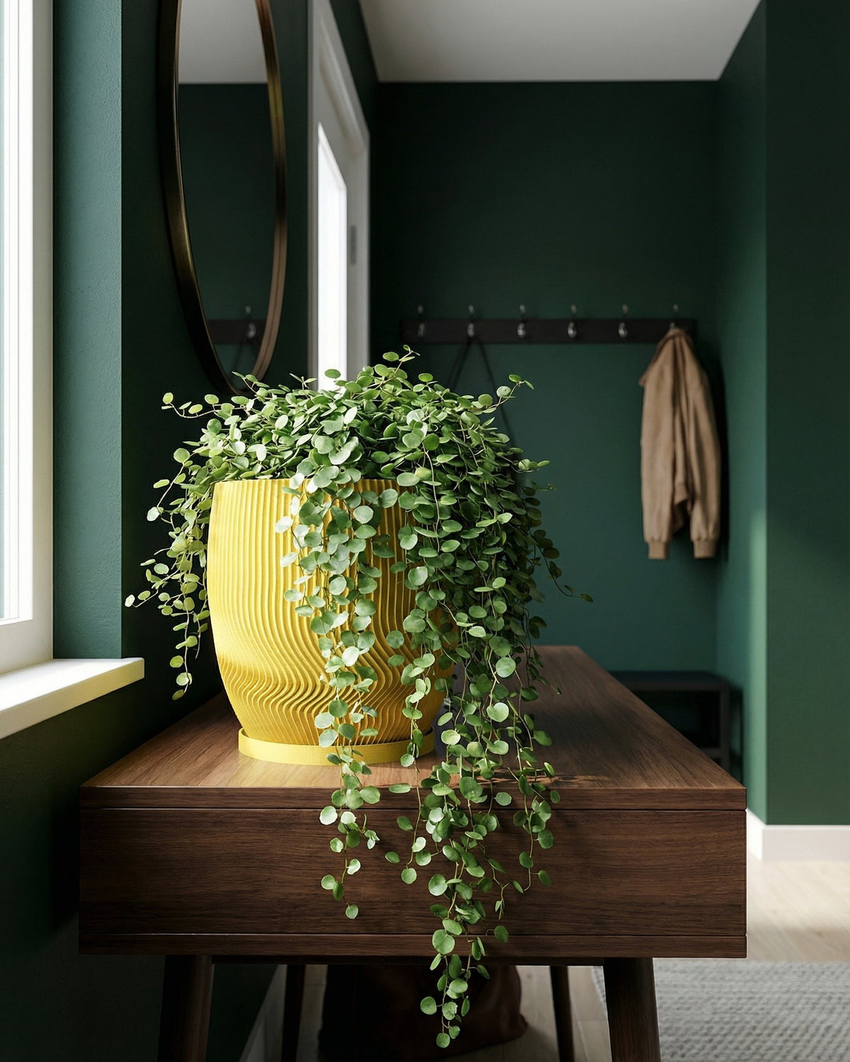 A vibrant yellow planter pot filled with a lush green trailing plant sits atop a dark wood console table in a room with dark green walls.