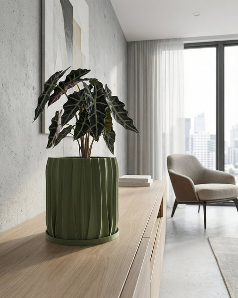 A green planter pot with a textured surface sits on a dark wooden table, filled with a lush green plant with variegated leaves. The background is a solid orange wall.