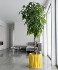 A yellow planter pot with a trailing plant sits on a wooden table next to a gray sofa. The pot has a textured, swirling design.