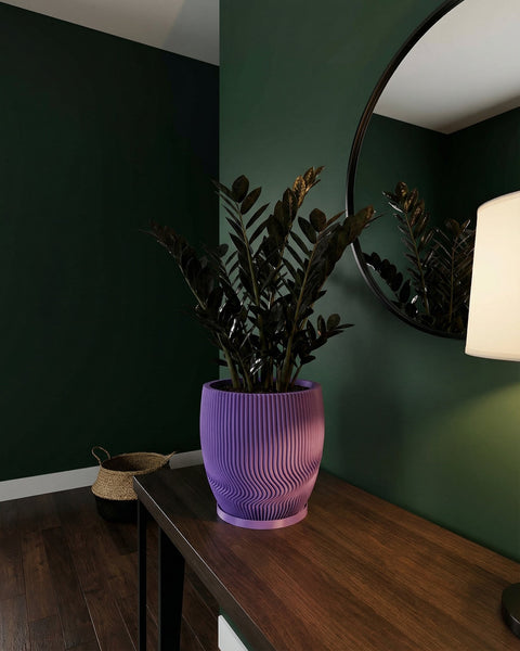 A purple planter pot with a plant inside sits on a wooden table, with a mirror and lamp nearby.