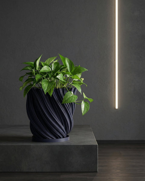 A dark blue planter pot with a textured, swirling design sits on a wooden cabinet, holding a green plant with round leaves.