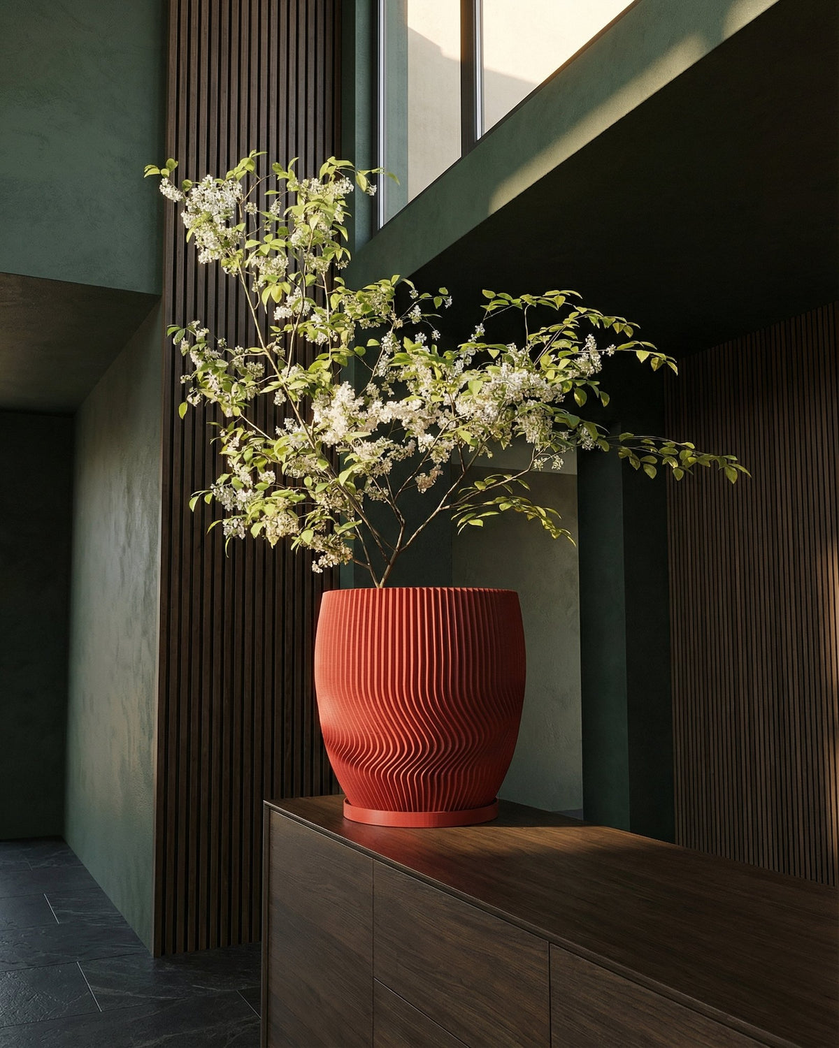 A red planter pot with a white flowering plant sits on a dark wood cabinet in a modern, minimalist room.