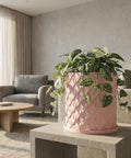 A pink planter pot with a plant inside sits on a dark wood cabinet with books and vases.