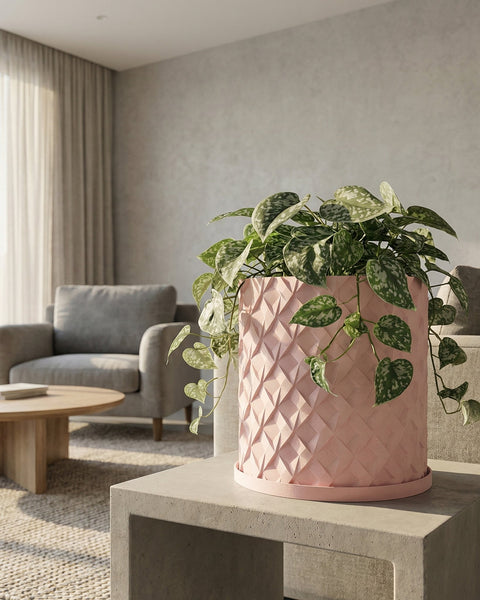 A pink planter pot with a plant inside sits on a dark wood cabinet with books and vases.